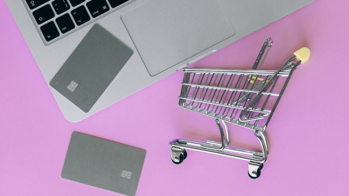 A minimalist flat lay of a credit card, laptop, and miniature shopping cart