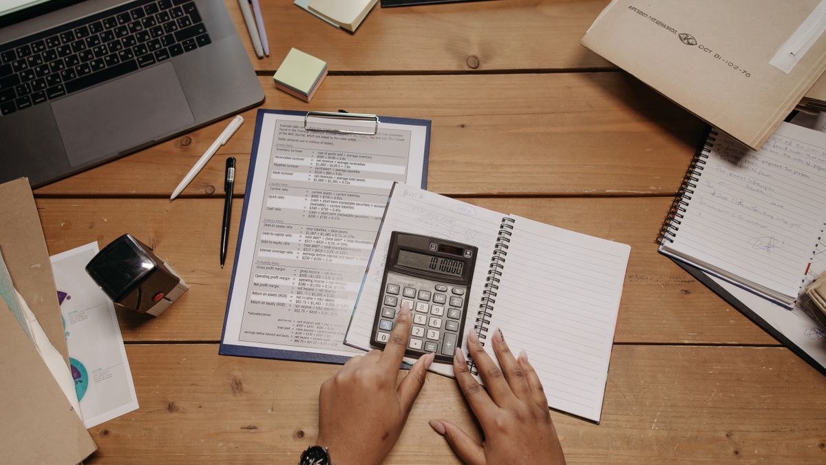 Hands working with calculator and documents on wooden desk in office setting