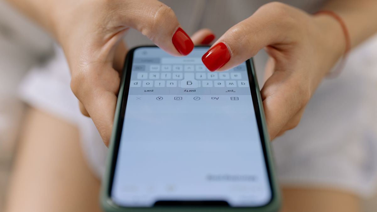 Close-up image of hands with red nails typing on a smartphone screen, showcasing modern technology