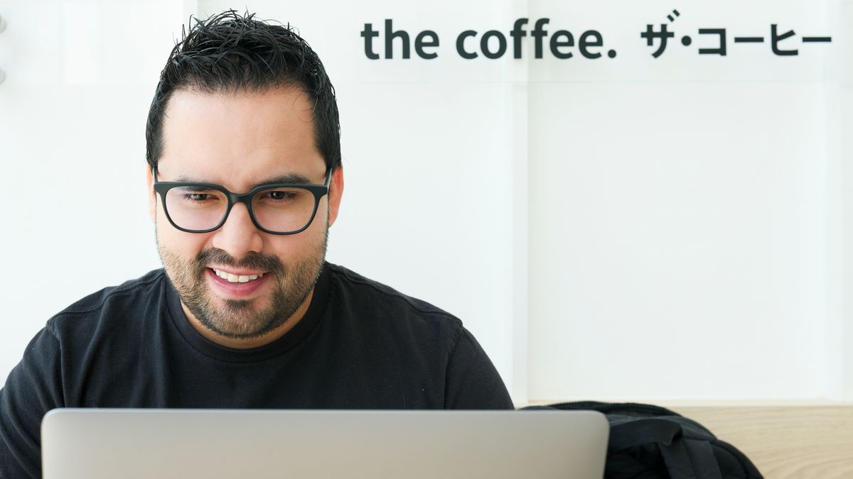 A smiling man using a laptop in a modern coffee shop setting indoors