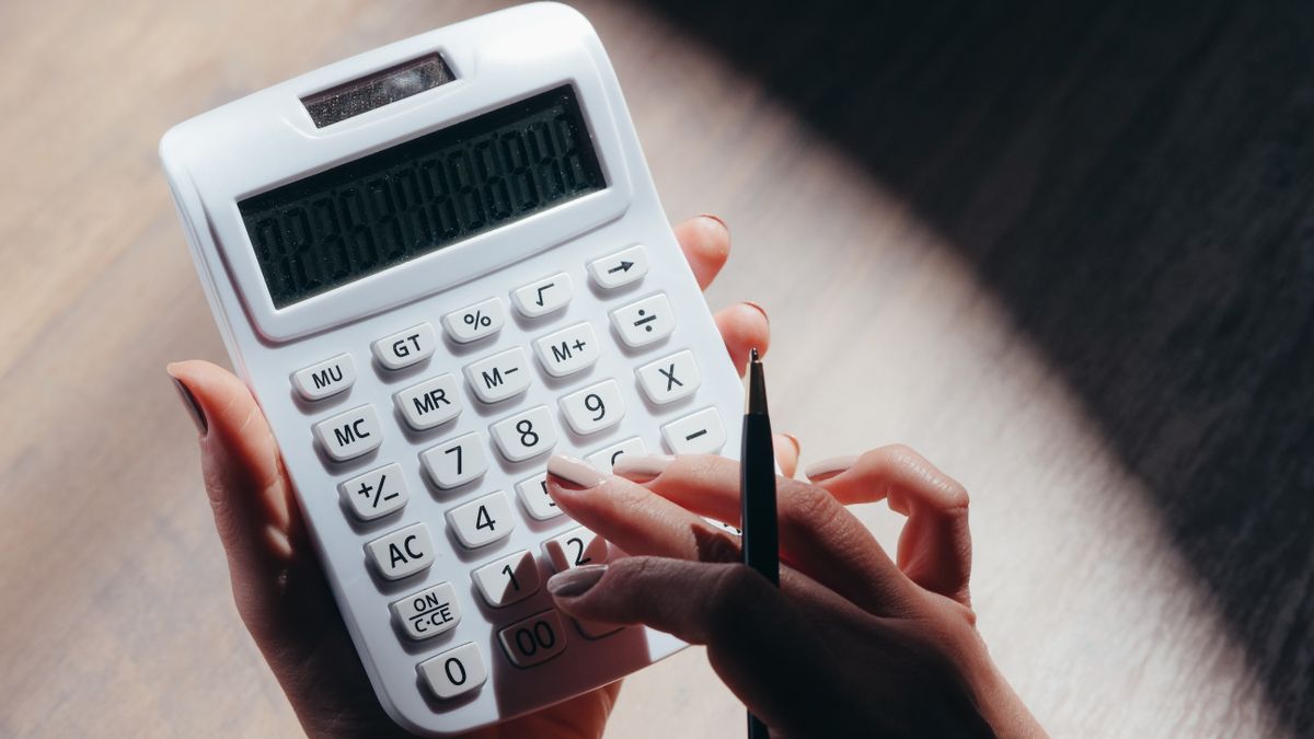 Hands holding a calculator and pen for financial calculations in a well-lit setting