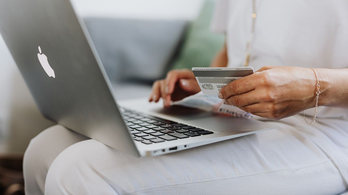 Close-up of a person holding a credit card while shopping online using a laptop at home