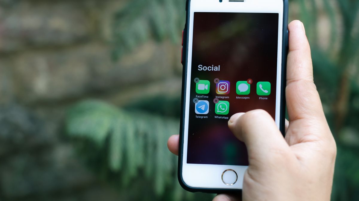 Close-up of a hand holding a smartphone displaying social media apps outdoors