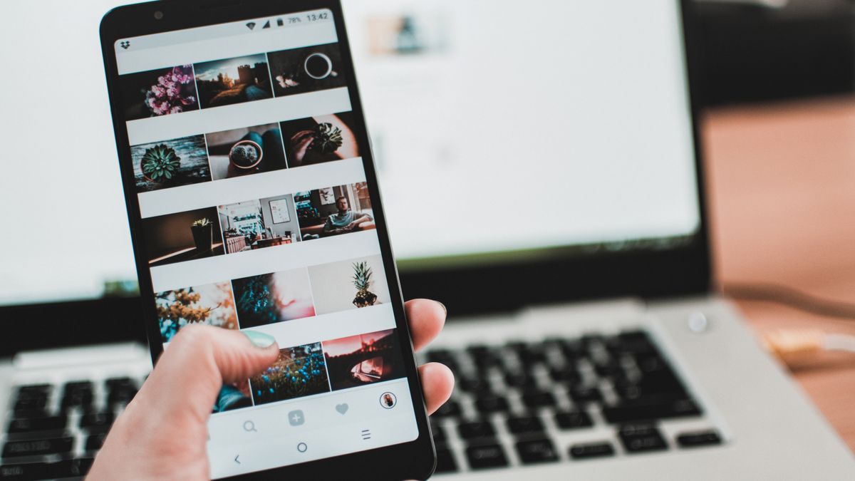 A person uses a smartphone to browse social media in front of a laptop, emphasizing modern technology and lifestyle