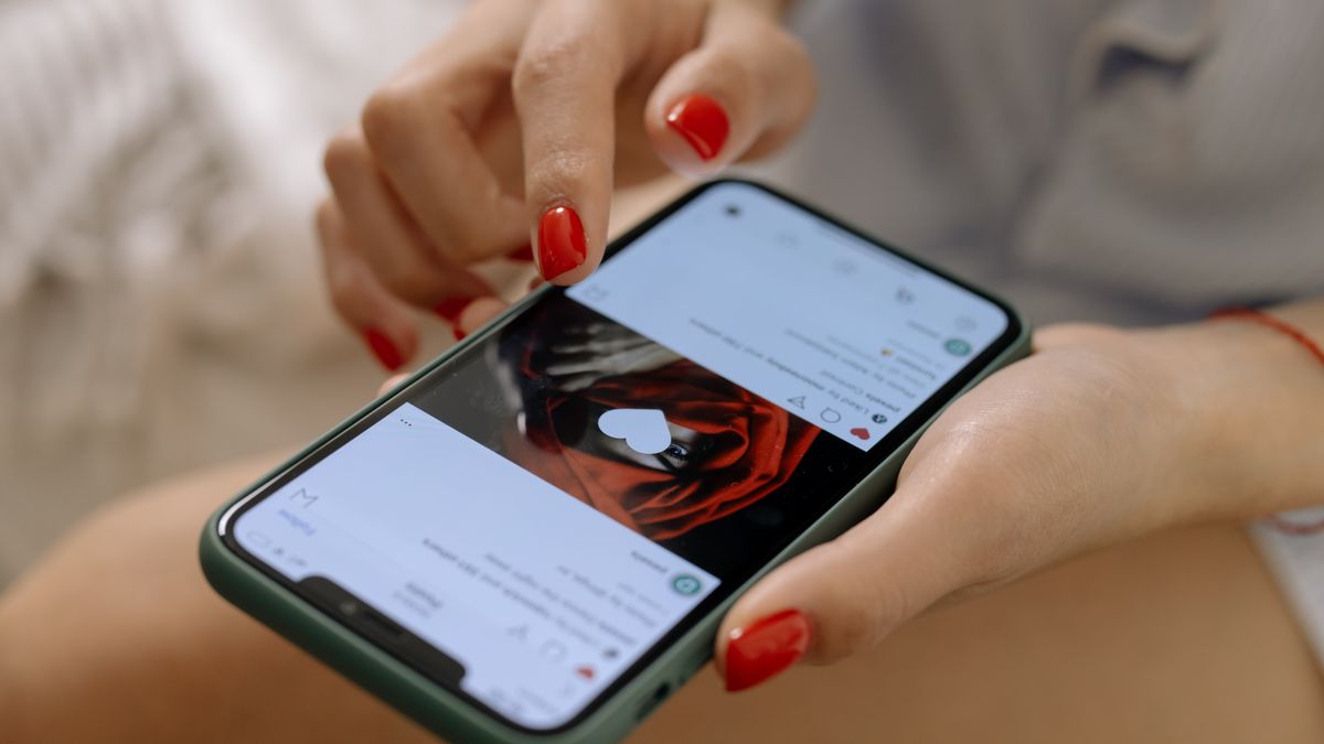 Close-up of a woman with red nails using a smartphone indoors, showcasing social media browsing