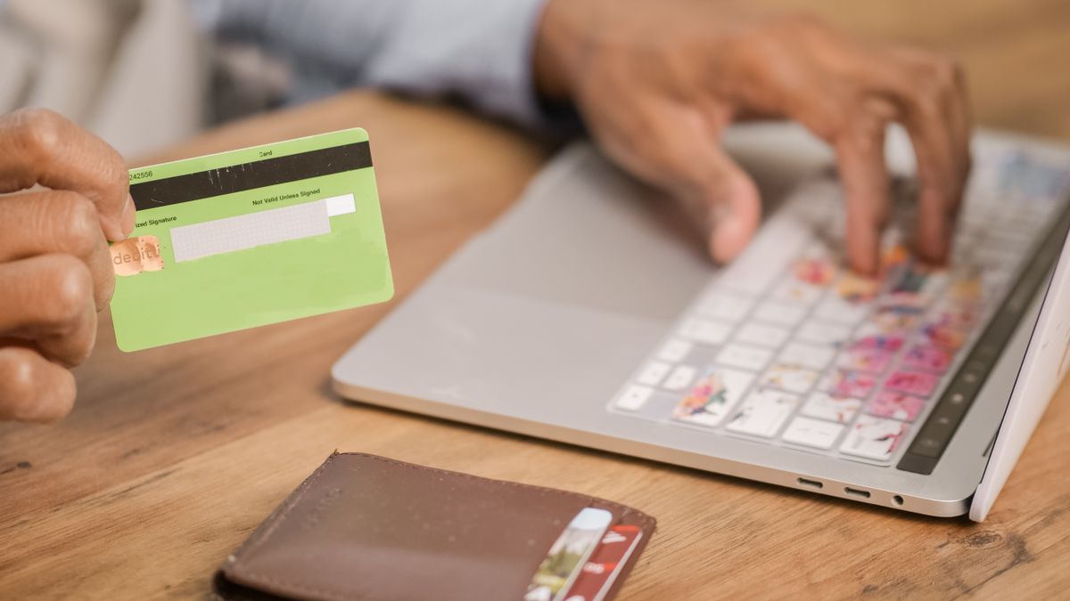 Person using a credit card for an online purchase on a laptop at a wooden table
