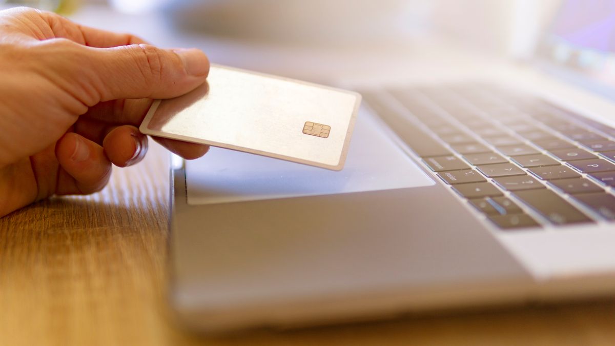 A person holds a credit card near a laptop for online shopping