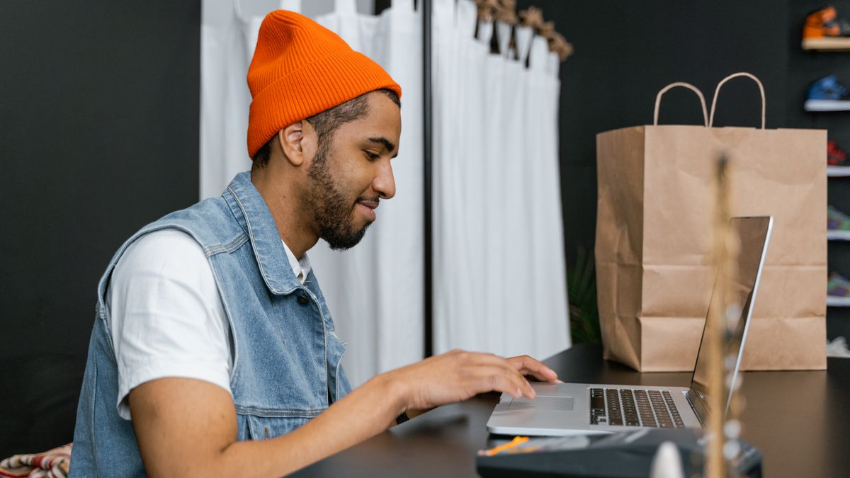 Man in a beanie using laptop in a stylish fashion store, indoors
