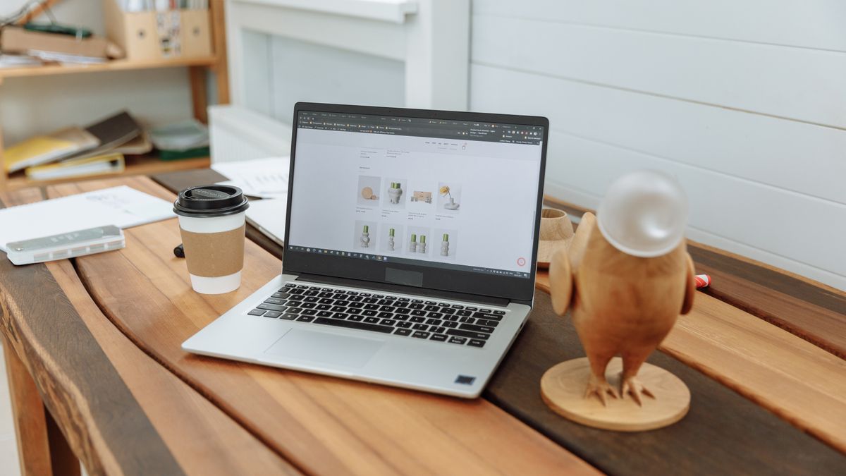 A contemporary office desk setup featuring a laptop, coffee cup, and wooden figurine on a wooden table
