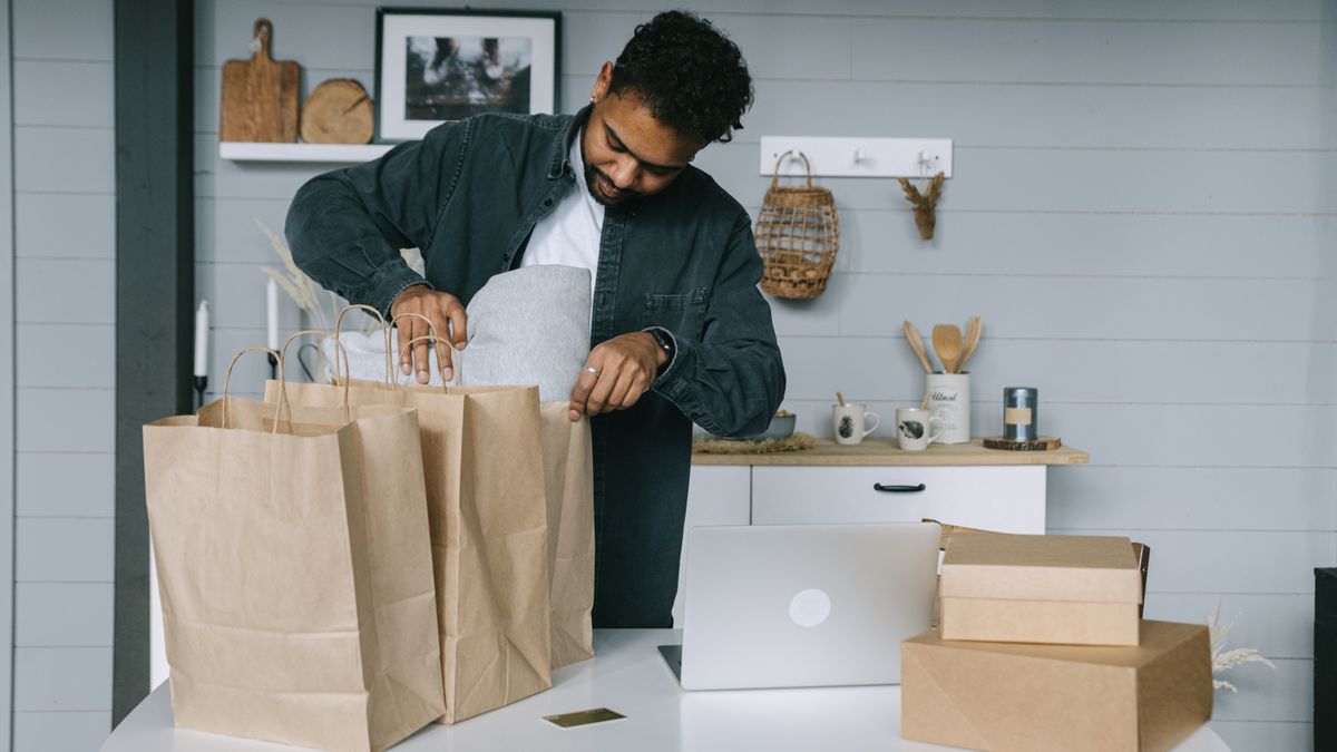 Young man organizing paper bags near a laptop in a cozy indoor setting