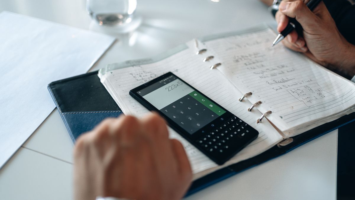 Close-up of hands writing in notebook with smartphone calculator on the table
