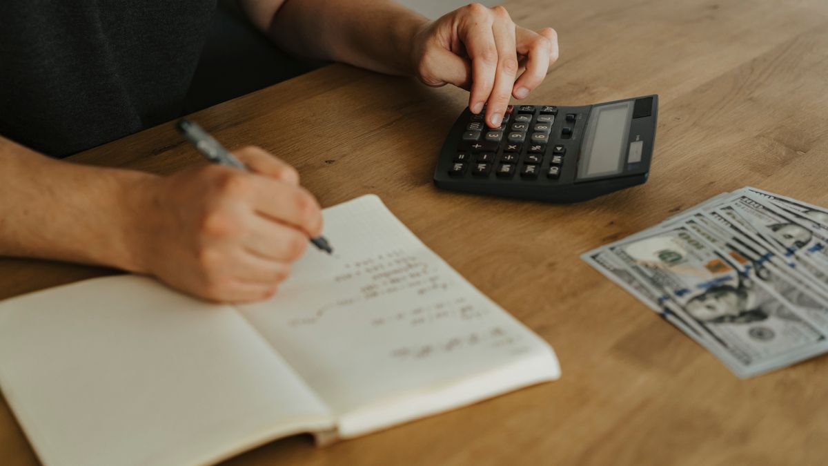 Close-up of hands using a calculator with notebook and cash on a wooden table