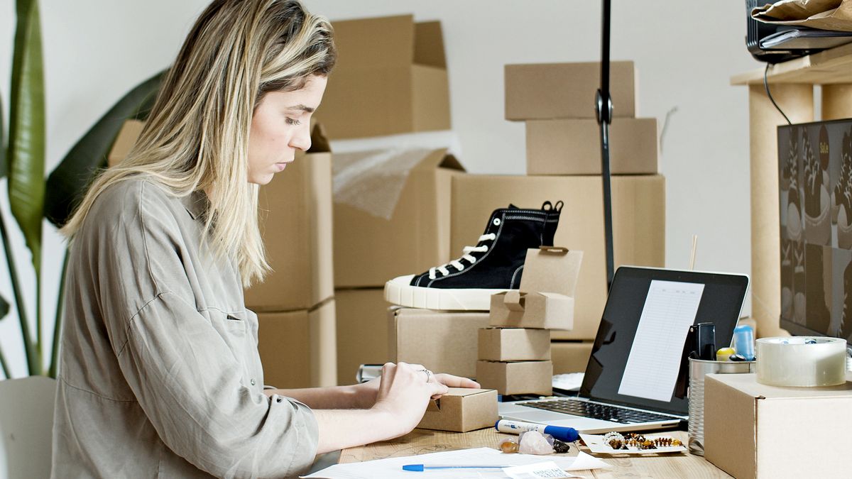 A woman packing boxes for her online store, surrounded by packaging materials and a laptop